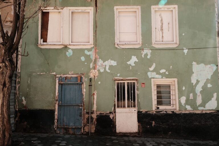 An abandoned building with green peeling paint and boarded windows.