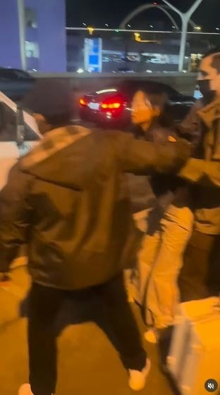 一名在现场自报姓名为「Jing Zhao」的华人女子,在机场航站楼外被多名便衣人员控制并带上一辆白色厢型车。面对旁人的追问,现场人员确认自己属于美国移民与海关执法局(ICE),并称带走女子的原因是「违反移民规定」。(IG@veganchefchristucker影片截图)