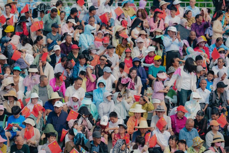 A densely packed crowd with flowers and flags fills a vibrant stadium, exuding excitement.