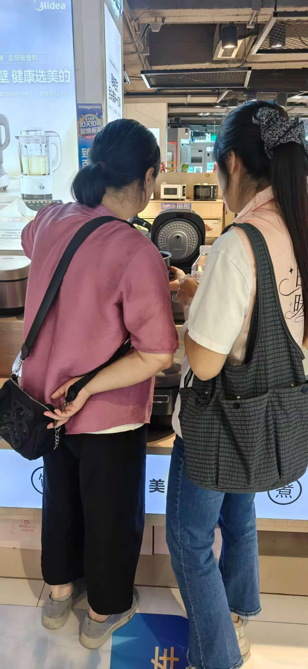 养老陪伴师陪老人家话家常,也帮忙跑腿、代办、陪诊、陪买家电等。图为“时光伴客”平台的陪伴师(右)陪同长者在商场挑选电饭煲。(受访者提供)