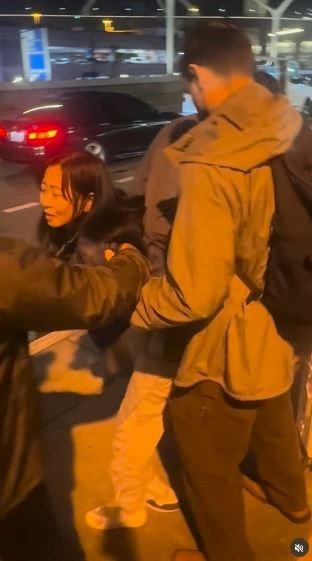 一名在现场自报姓名为「Jing Zhao」的华人女子,在机场航站楼外被多名便衣人员控制并带上一辆白色厢型车。面对旁人的追问,现场人员确认自己属于美国移民与海关执法局(ICE),并称带走女子的原因是「违反移民规定」。(IG@veganchefchristucker影片截图)